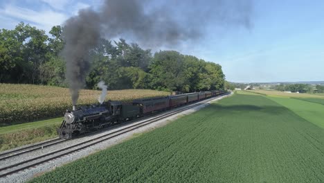 Vista-Aérea-De-Un-Tren-De-Pasajeros-De-Vapor-Que-Sale-De-Una-Estación-De-Tren-En-El-Campo-Amish-En-Un-Día-De-Verano