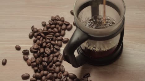 Pouring-fresh-coffee-into-a-pot-with-coffee-beans-background