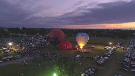 Luftaufnahme-Eines-Heißluftballonfestivals-Bei-Nacht,-Bei-Dem-Propan-Abgefeuert-Wird-Und-In-Einer-Sommernacht-Ein-Nächtliches-Leuchten-Erzeugt