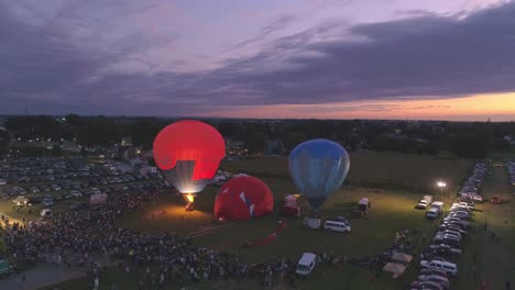 Vista-Aérea-De-Un-Festival-De-Globos-Aerostáticos-Por-La-Noche-Disparando-Propano-Creando-Un-Resplandor-Nocturno-En-Una-Noche-De-Verano