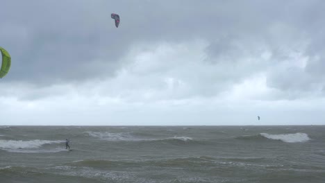 Kitesurfer,-Die-Auf-Den-Großen-Ostseewellen-Am-Strand-Von-Liepaja-Karosta-Segeln,-Bewölkter-Herbsttag,-Weite-Aufnahme-In-Zeitlupe