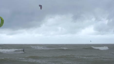 Kite-surfing-surfers-sailing-on-the-big-Baltic-sea-waves-at-Liepaja-Karosta-beach,-overcast-autumn-day,-slow-motion-wide-shot