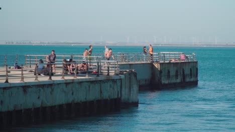 Slowmo,-Two-boys-jump-off-pier-into-ocean-water-in-Bay-of-Cadiz,-Spain