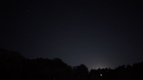 Motion-Time-Lapse-of-night-sky-with-stars-and-the-moon-hiding-in-the-silhouette-of-a-forest