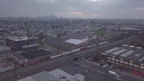 Aerial-view-of-Philadelphia-Industrial-section-with-trains-passing-skyline-in-distance