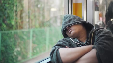 Un-Hombre-Japonés-Se-Cubrió-La-Cara-Con-Su-Sudadera-Con-Capucha-Durmiendo-En-Un-Tren-En-Movimiento-En-Tokio,-Japón---Plano-Medio