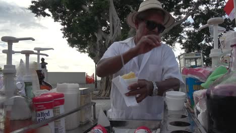 Man-pouring-syrup-into-a-snow-cone---selling-it-to-someone-handing-over-currency