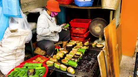 Saigon-Woman-Grilling-Street-Food-Wrapped-In-Banana-Leaves-In-Ho-Chi-Minh,-Vietnam---close-up-slowmo
