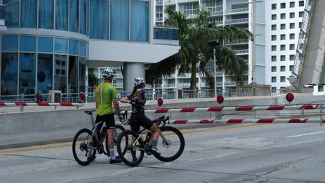 Pareja-De-Ciclistas-Esperando-En-Una-Rampa-Cerrada-Frente-Al-Puente-Levadizo-En-El-Centro-De-Miami-Durante-El-Brote-De-Covid-19,-Florida-Usa,-50fps