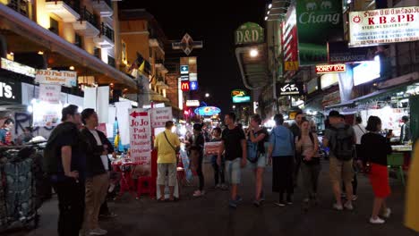 Handheld-scenes-of-the-tourists-are-walking-around-Khao-San-Road-at-night-time-famous-which-each-year-tourists-from-many-countries-came-to-visit-in-Bangkok,-Thailand