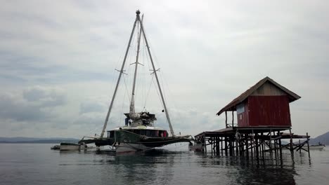 Velero-Trimarán-Bigkanu-Atracado-En-Una-Cabaña-De-Buceo-En-Un-Arrecife-Oceánico-Pintado-De-Rojo,-Círculo-Aéreo-Alrededor-Del-Tiro