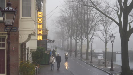 A-yellow-hotel-sign-on-a-street-in-Amsterdam-on-a-misty-foggy-day-with-people-walking-past