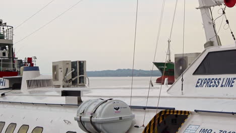 Sochi-expresses-a-ferry-boat-in-the-foreground,-as-a-huge-cargo-ship-passing-by-in-the-background-sailing-out-from-a-port