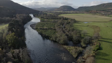 Aerial-view-flying-over-the-River-Dee-towards-Ballater-in-the-Cairngorms-National-Park-on-a-sunny-day,-Aberdeenshire