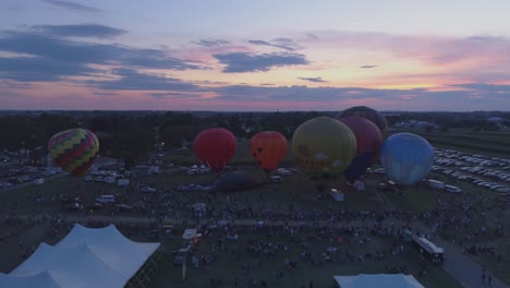 Luftaufnahme-Von-Heißluftballons,-Die-Sich-Für-Eine-Nächtliche-Flammenshow-Bei-Einem-Ballonfestival-Bei-Sonnenuntergang-Füllen,-Wie-Von-Einer-Drohne-Gesehen