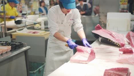 Hombre-Experto-Cortando-Atún-Rojo-Fresco-En-Diferentes-Porciones-Con-Gente-Mirando-En-Un-Mercado-De-Pescado-En-Toretore-Ichiba,-Wakayama-Japón