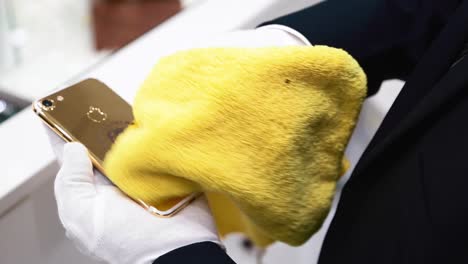 Manos-Con-Guantes-Blancos-Limpiando-Un-Donald-Trump-Iphone-7-Chapado-En-Oro-Usando-Un-Paño-Amarillo---Tiro-De-ángulo-Alto