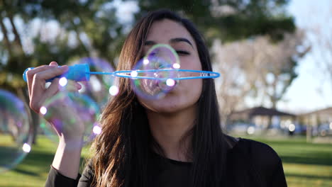 Close-up-of-a-happy-young-woman-playing-and-smiling-while-blowing-bubbles-in-the-dreamy-park-sunlight