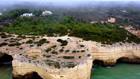 Cuevas-Talladas-En-El-Mar-De-La-Playa-De-Fontainhas-En-Portugal-Con-Furgoneta-De-Camping-En-La-Parte-Superior,-Plataforma-Rodante-Aérea-En-Toma-De-Revelación