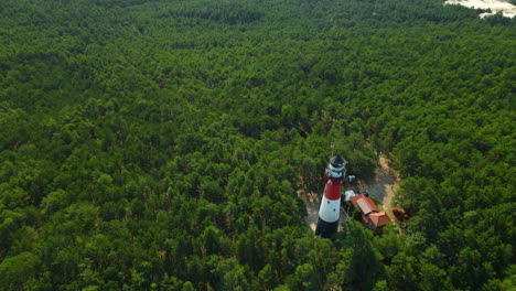 Incredible-White-and-red-light-House-stands-tall-above-trees-in-a-dense-forest-as-a-drone-circle-orbits-around