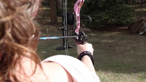 Woman-shooting-a-compound-bow-in-a-grass-backyard