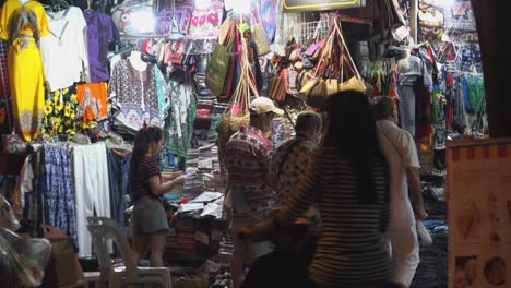 Medium-Exterior-Still-Shot-of-Tourists-Exploring-Night-Market-Wile-Seller-Sorts-Out-Her-Sock-From-Across-a-Road-in-the-Night-Time