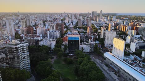 Dolly-out-flying-over-Barrancas-de-Belgrano-park-and-train-station-surrounded-by-buildings-at-sunset,-Buenos-Aires,-Argentina