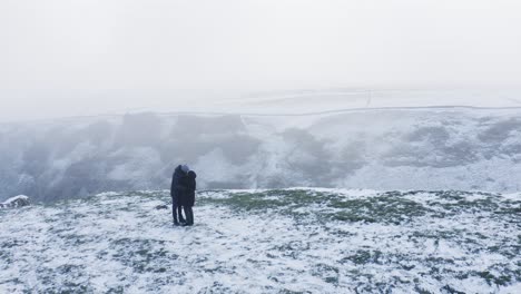 Young-couple-kiss-on-the-top-of-a-snow-capped-mountain,-Winnats-Pass,-Peak-District