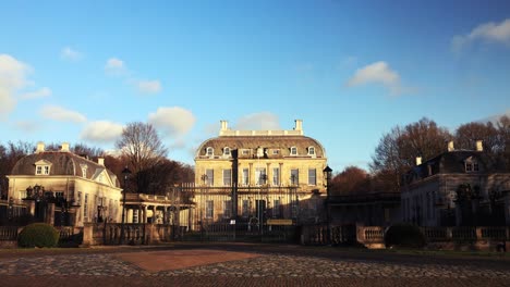 Zeitraffer-Des-Wasserschlosses-Huis-De-Voorst-Manor,-Das-Flüchtige-Wolken-Und-Vorbeiziehende-Fußgänger-Vor-Einem-Blauen-Himmel-Bei-Sonnenuntergang-Zeigt