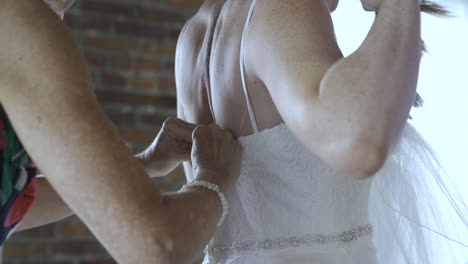 Bridesmaid-closes-back-of-bride's-wedding-dress-and-adjust-straps