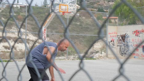 Close-view-from-behind-a-chain-link-fence-of-a-man-playing-basketball-at-an-outdoor-court