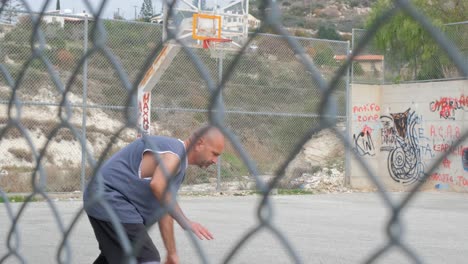 Nahansicht-Hinter-Einem-Maschendrahtzaun-Eines-Mannes,-Der-Auf-Einem-Außenplatz-Basketball-Spielt