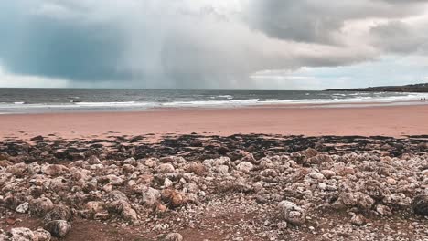 Empty-rocky-beach-on-a-cold-winters-day-in-South-Shields,-UK-with-stormy-grey-rain-clouds