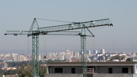 Construction-Site-of-high-rise-building-with-green-cranes-and-workers-on-rooftop