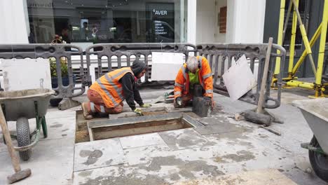 Two-male-workers-in-high-vis-jackets-installing-pavement-in-central-london