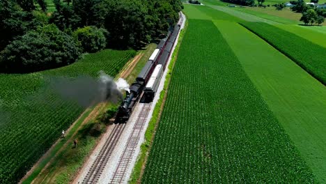 Steam-Train-at-Picnic-Area,-Dropping-off-Passengers-as-Second-Steam-Train-Passes,-in-Amish-Countryside-as-seen-by-Drone