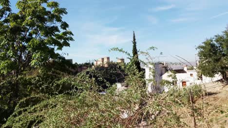 The-famous-Alhambra-appears-in-a-distance,-behind-a-cobblestone-wall,-while-the-camera-trucking-slightly-upwards