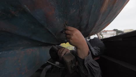 Pescador-Griego-Restaurando-La-Parte-Inferior-Del-Casco-Del-Barco-De-Pesca-Construido-Carvel-Martillando-La-Vieja-Masilla-De-Lechada