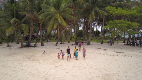 Toma-Aérea-Estática-De-Un-Joven-Caucásico-Y-Niños-Filipinos-Saludando-A-Un-Dron-Desde-Una-Hermosa-Isla-Con-Palmeras-En-Filipinas