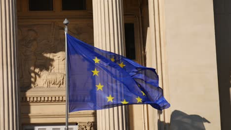 European-flag-moving-in-the-wind-in-front-of-a-building-inspired-by-antique-Greece-columns-with-its-shadow-on-a-wall