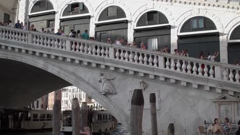 Famoso-Monumento-Italiano,-El-Puente-De-Rialto-Con-Turistas-Visitando---Barcos---Góndolas-Que-Pasan-Por-Debajo