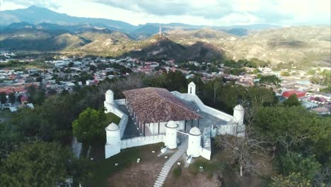 AERIAL-SLOW-MOTION:-Aerial-slow-motion-pan-shot-of-fortress-on-hilltop-sorrounded-by-trees-and-overlooking-city