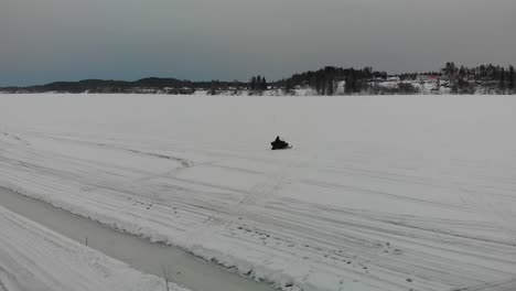 Toma-Aérea-De-Seguimiento-De-Un-Hombre-Conduciendo-Su-Moto-De-Nieve-En-Indalsalven-En-Timra,-Sundsvall,-Suecia