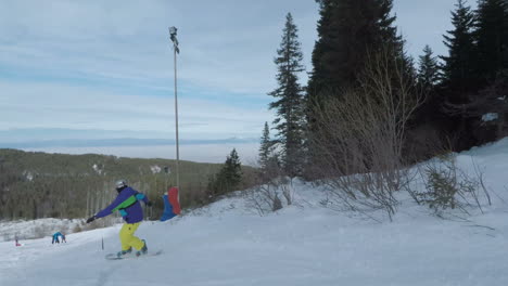 Snowboarder-heading-off-down-white-slopes-at-resort-in-between-other-boarders---skiers