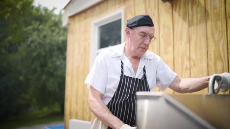 Older-chef-cooking-burgers-and-hotdogs-on-a-barbecue-outside