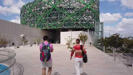 Schwenk-Nach-Rechts,-Während-Zwei-Personen-An-Der-Kamera-Vorbei-Zum-Großen-Museum-Der-Maya-Welt-In-Merida,-Yucatan,-Mexiko-Gehen