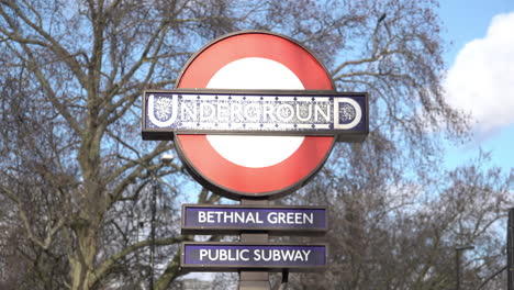 Großbritannien,-Februar-2019-–-Wolken-Ziehen-Vorbei-Und-Ein-Vogel-Landet-Auf-Einem-Laternenpfahl-Hinter-Einem-Verwitterten-Roten,-Weißen-Und-Blauen-U-Bahn-Schild-Für-Den-Bahnhof-Bethnal-Green-Im-Osten-Londons