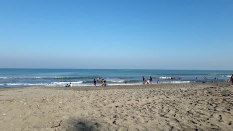 extreme-wide-shot-of-people,-young-and-adult-alike,-enjoying-the-waves-near-the-shoreline-of-a-public-beach