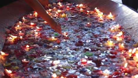 Tiro-Inclinado-De-Coloridas-Velas-Flotantes-Que-Muestran-Solo-Las-Manos-De-Algunas-Personas-Encendiendo-Sus-Velas-Y-Haciendo-Su-Oración-Silenciosa