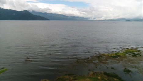 AERIAL:-Panoramic-shot-of-lake-sorrounded-by-mountains-and-blue-sky,-Yojoa,-Honduras